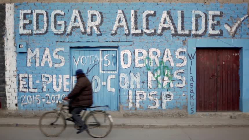 A bicyclist rides by a building with painted text on the side
