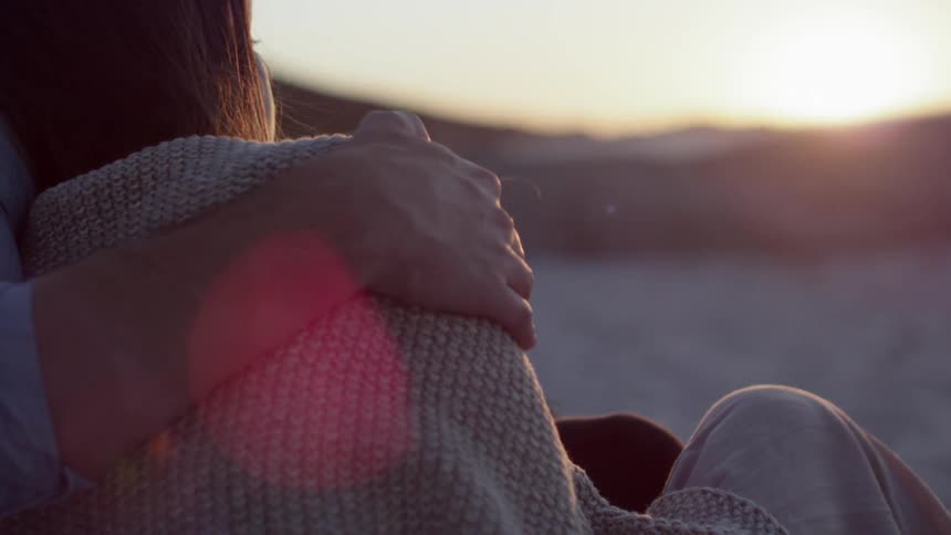 A man rubs a woman's shoulder at sunset