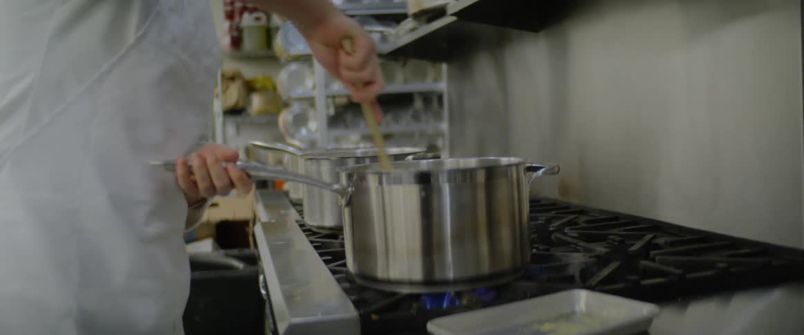 A chef stirs a pot on the stove in a restaurant kitchen