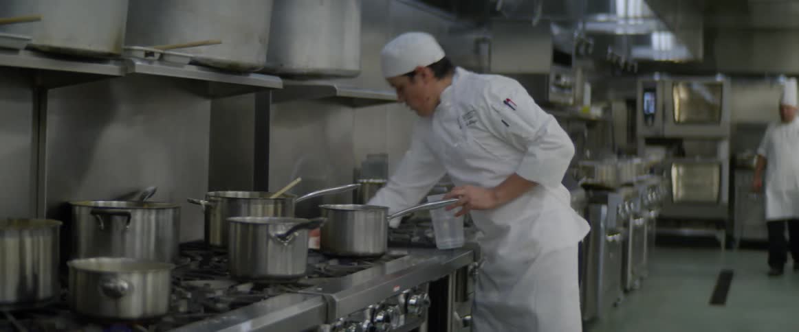 Sous chef cleaning stove with white rag in kitchen of a restaurant
