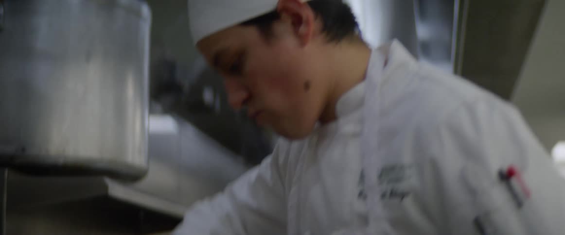 A cook stirring and shaking a pot on an oven in a commercial kitchen
