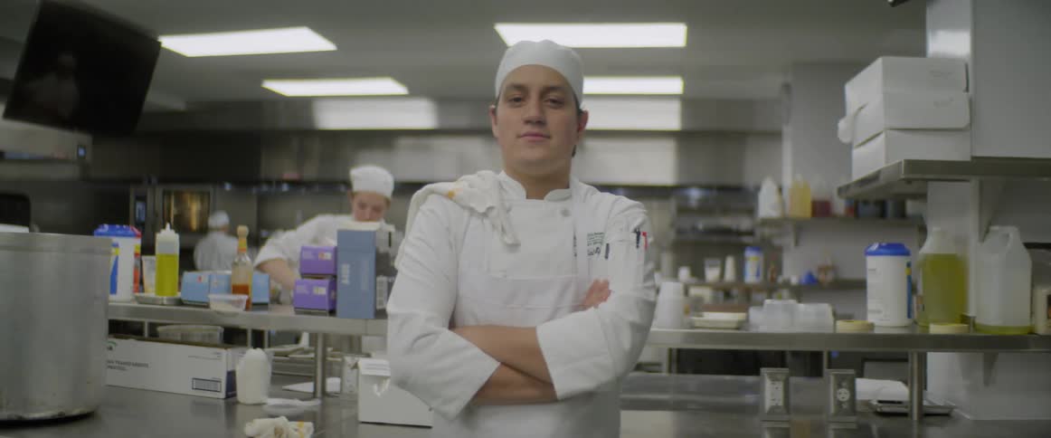 A chef flips a towel over his shoulder in a restaurant kitchen