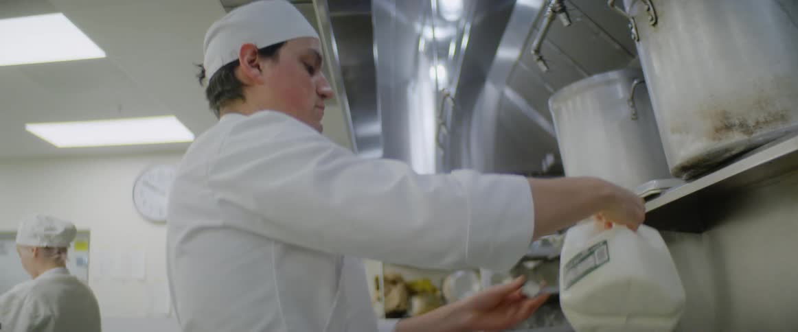 A chef pours milk in a pot in a restaurant kitchen