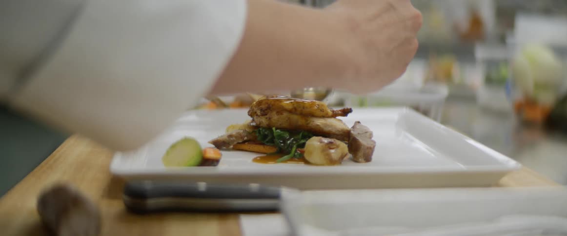 Close up of a chef spooning glaze over a gourmet meal