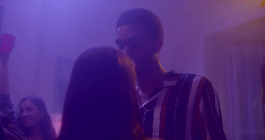 A young woman dances close to a young male amidst a crowded club lit with purple lights
