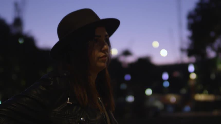 A woman stands around at night then takes her phone from her jacket pocket