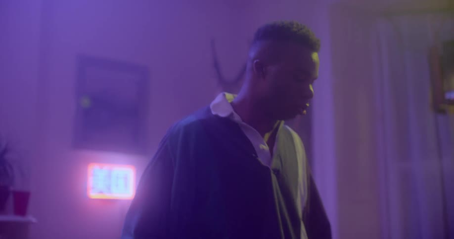 A black man dancing in a room illuminated by purple light
