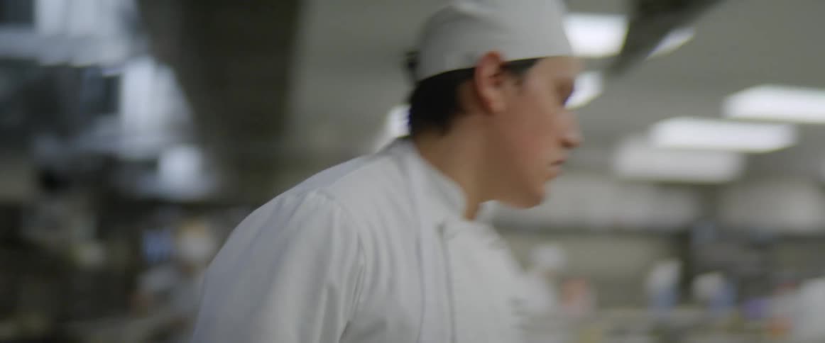 A chef adds chopped vegetables into a pot on the stove in a commercial kitchen