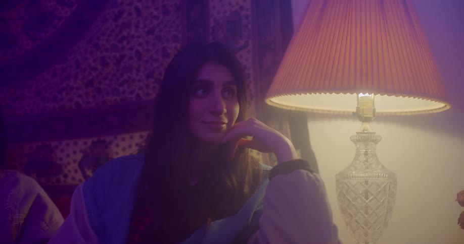 A woman nods her head while listening to someone while sitting in a living room behind a decorative tapestry
