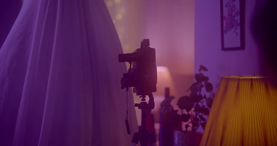 A camera sits on a tripod next to a figure under a sheet