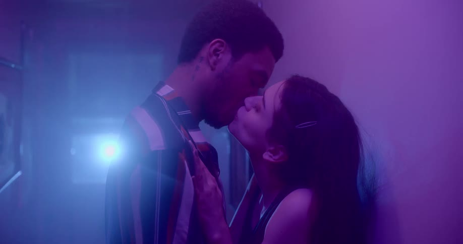 A man and woman make out in the hallway while headlights shine through a door