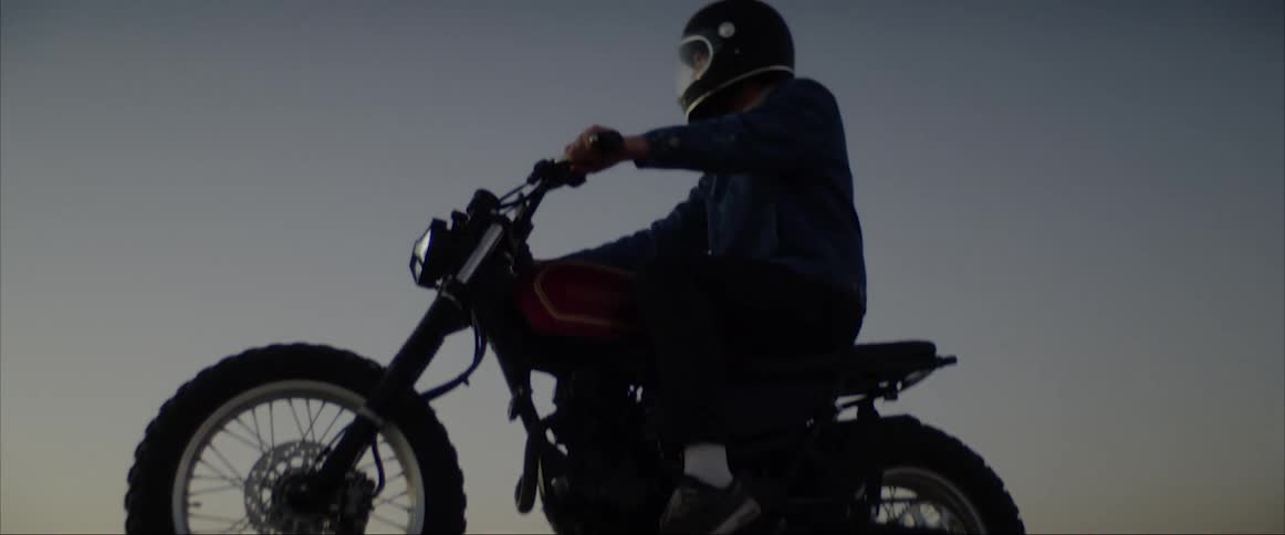 A man sits on a motorcycle on a sandy hill