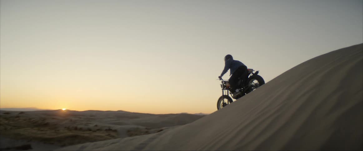 A person rides a motorcycle across a sand dune