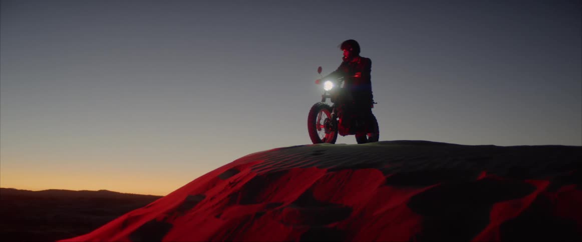 A person sits on a motorcycle on a sand dune in red light