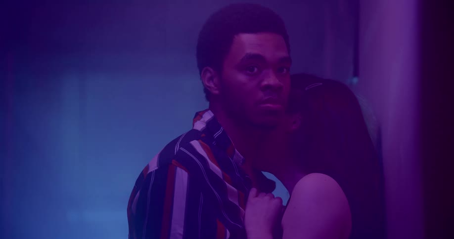 A man stares off to the side as a woman kisses his neck