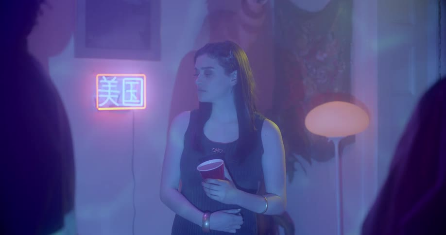 A woman sits in a room with flashing lights and people around with her eyes closed