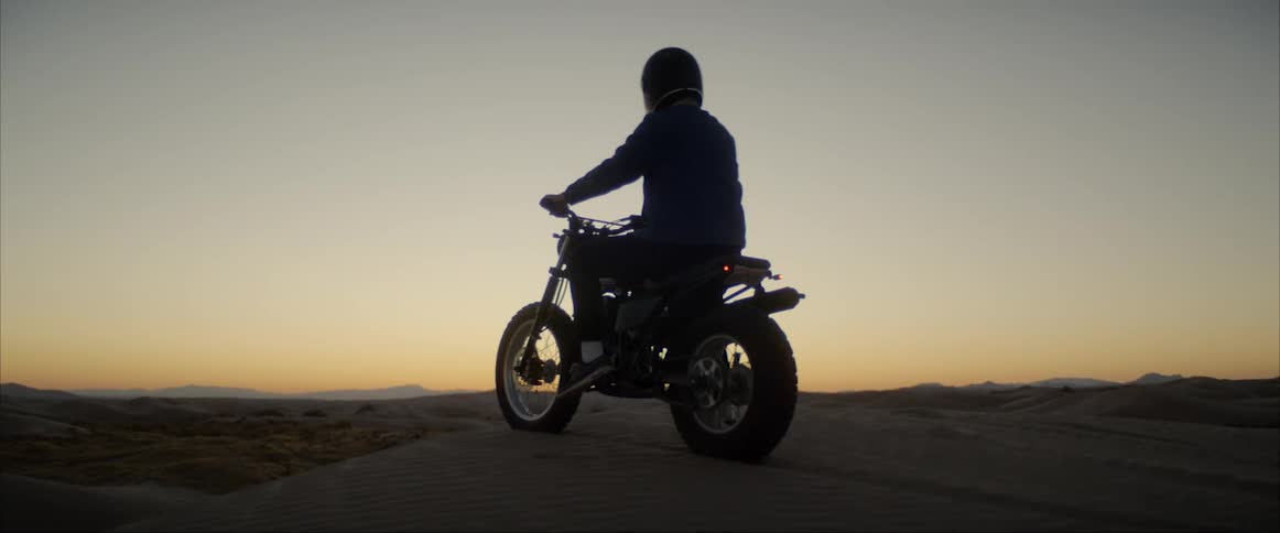 A person sits on a motorcycle on top of a sand dune