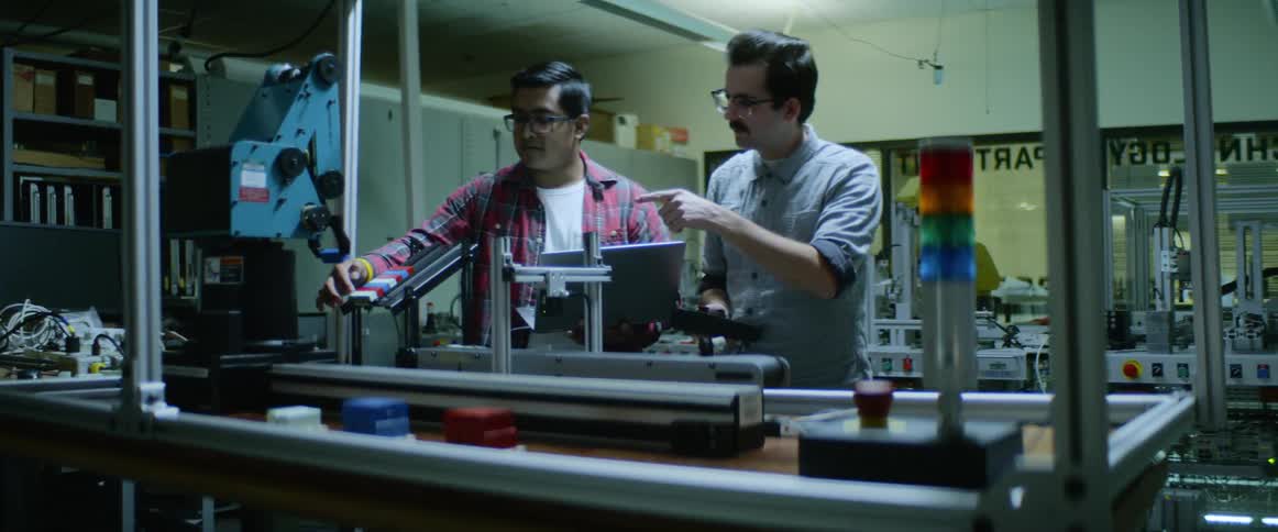 Two men stand in front of a large piece of technology equipment