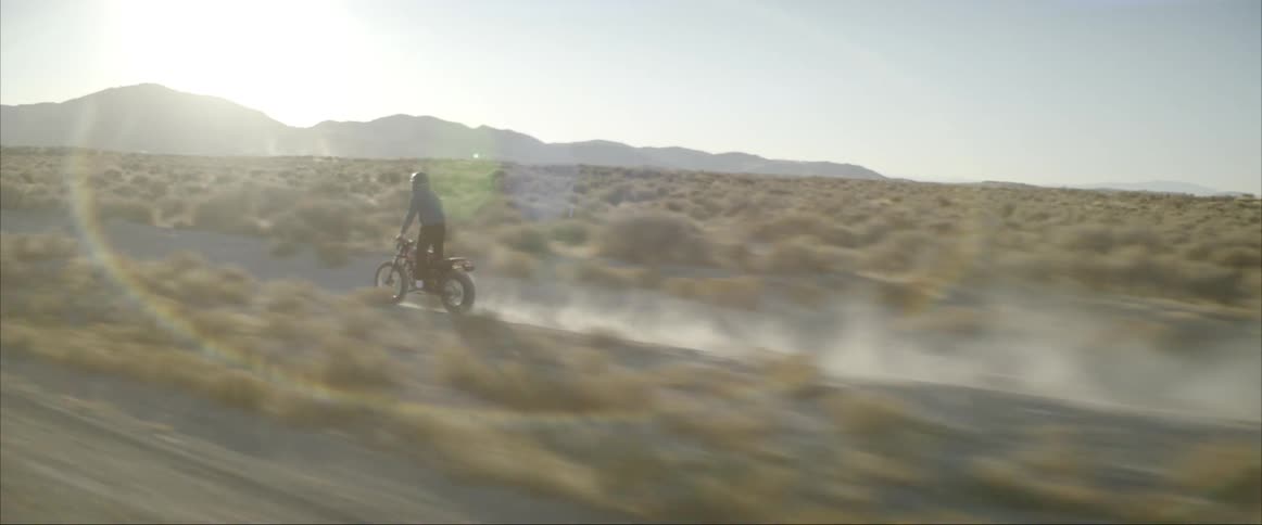 A motorcycle rider stands up as he drives on a dirt road in the desert