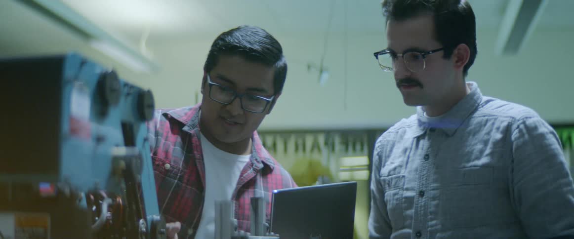 Two men standing in front of a robotic arm one holding a laptop