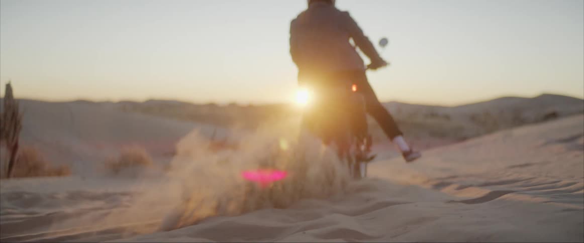 A person rides a motorcycle across sand in the desert