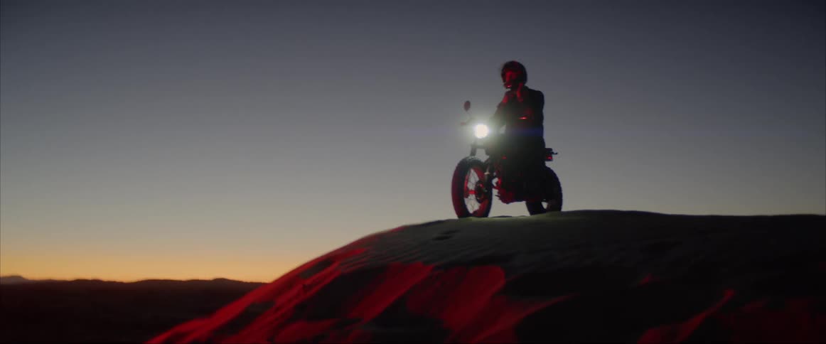 A man sits on his motorcycle on the top of a hill and puts his helmet on