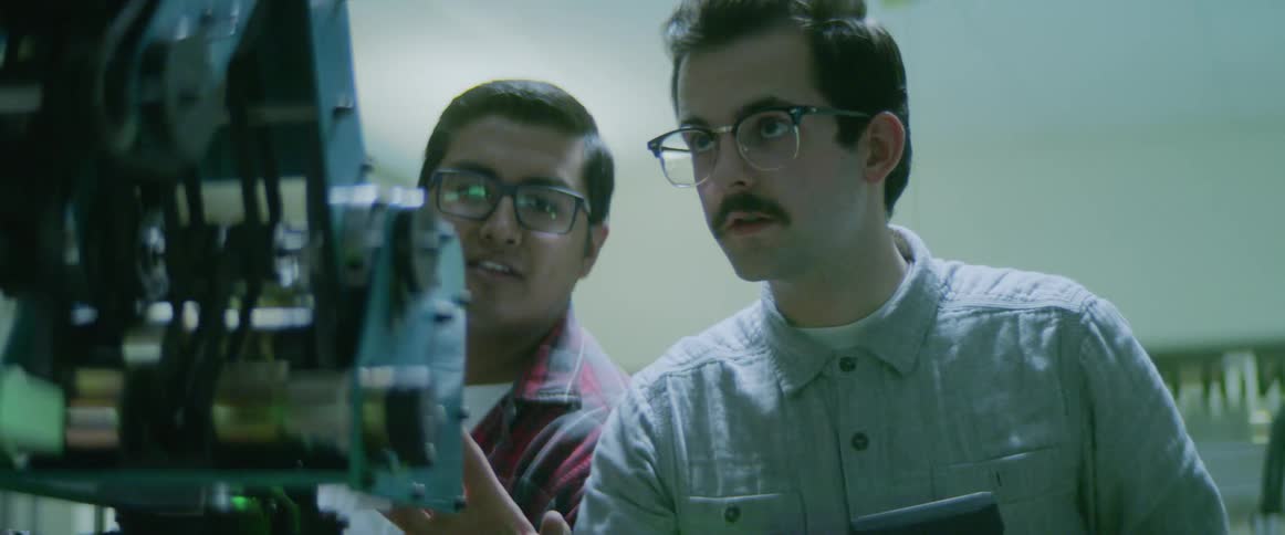 Two men look at a robotic machine as it turns around