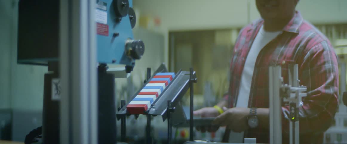Two men in front of a robotic arm one holding a laptop