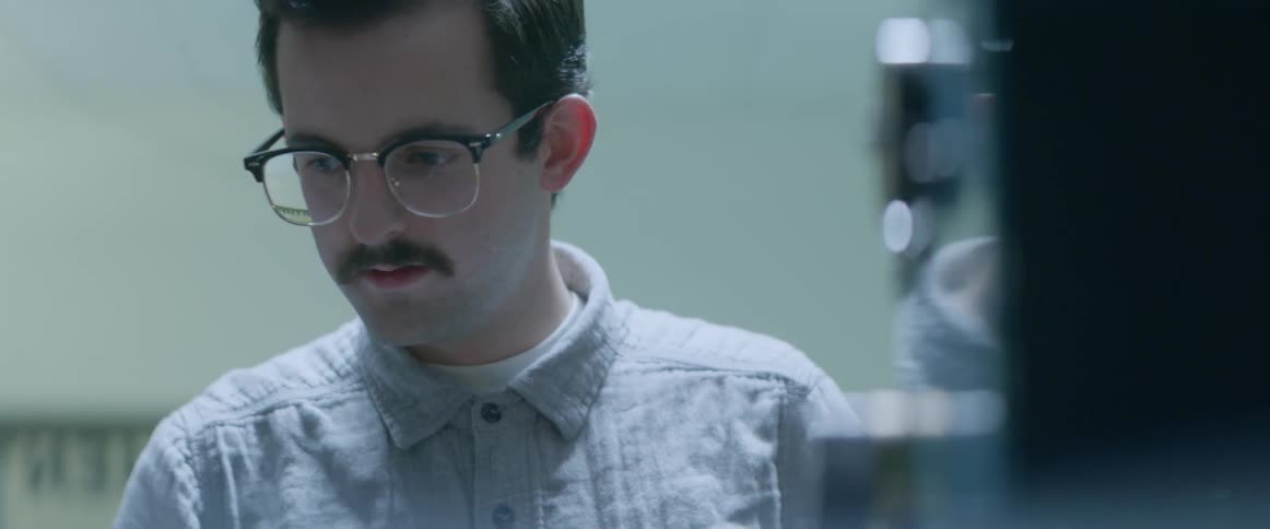 Two men in glasses talk to each other while looking at something