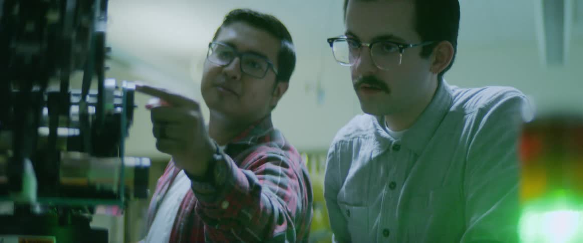 Two men talking in front of a robotic arm