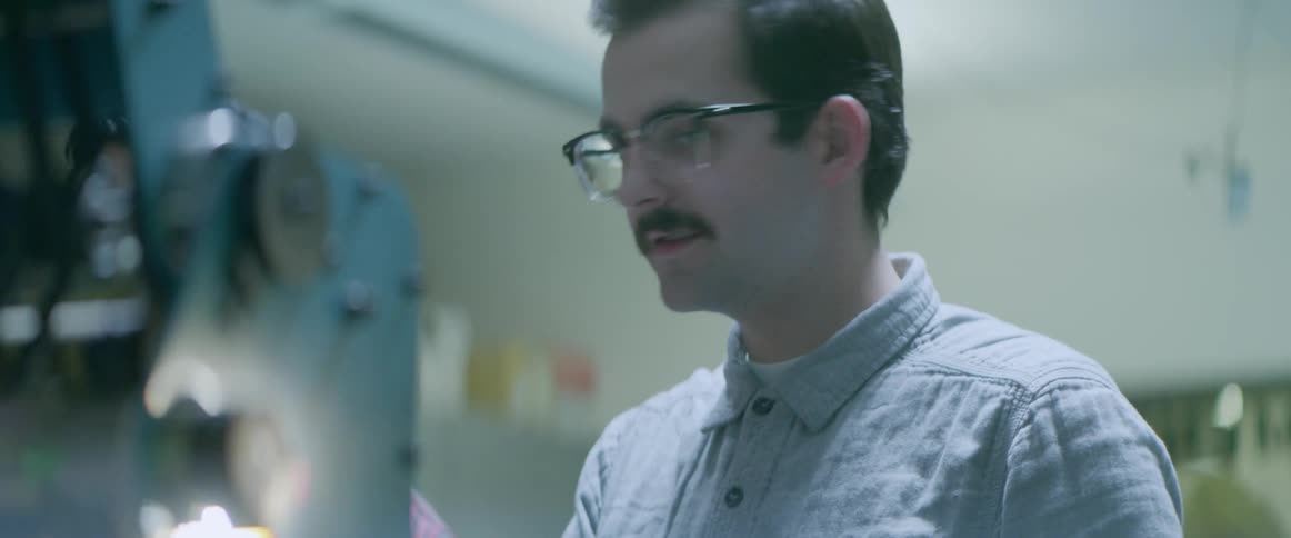 A man talks to another as he observes a robotic arm moving