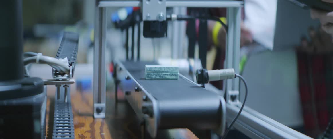 Two men standing in front of a robotic arm and a conveyor belt