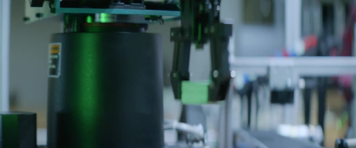 A robotic arm picks up pieces and moves them as two men watch