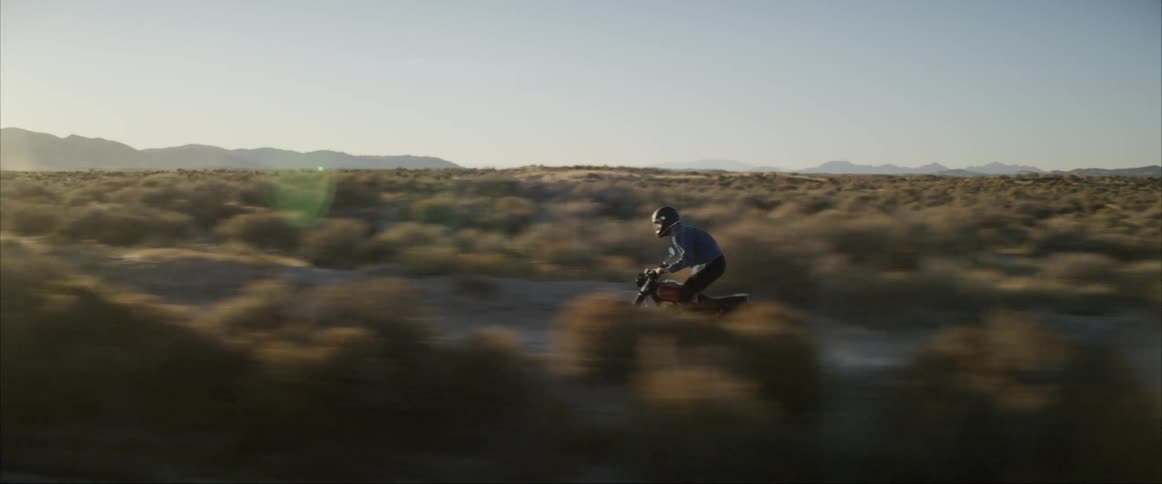 A motorcyclist speeds down a gravel road running through the desert