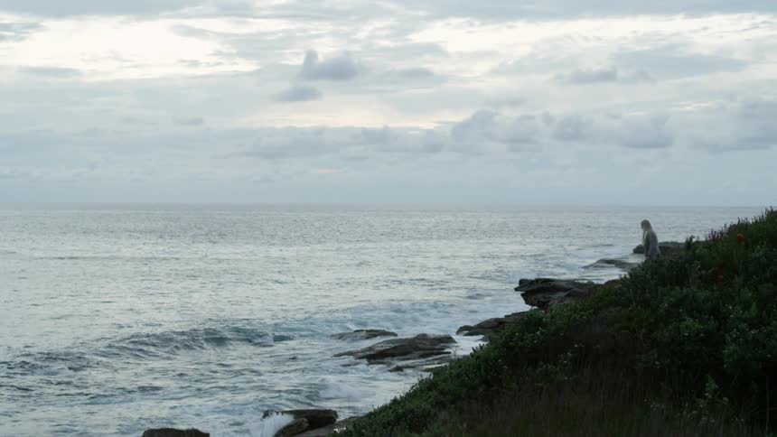 A woman walks out on a rock on a shoreline