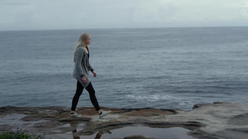 A woman walks on a rocky coastline