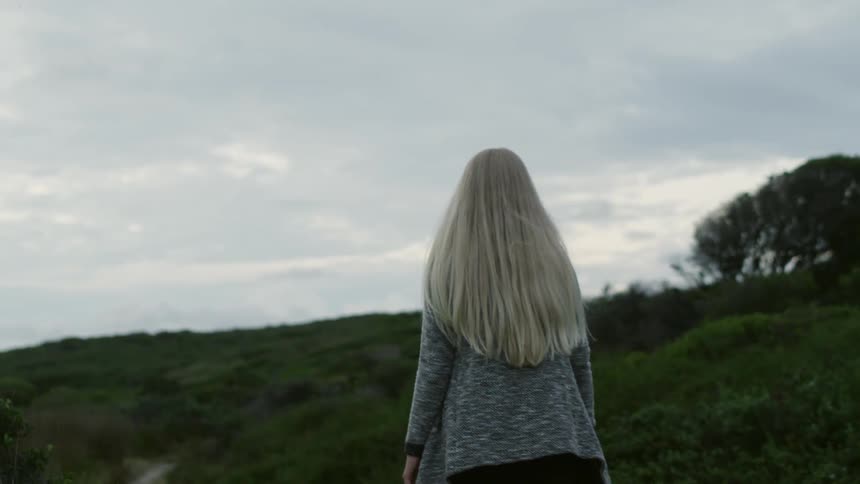 A woman walks up a hill on a cloudy day