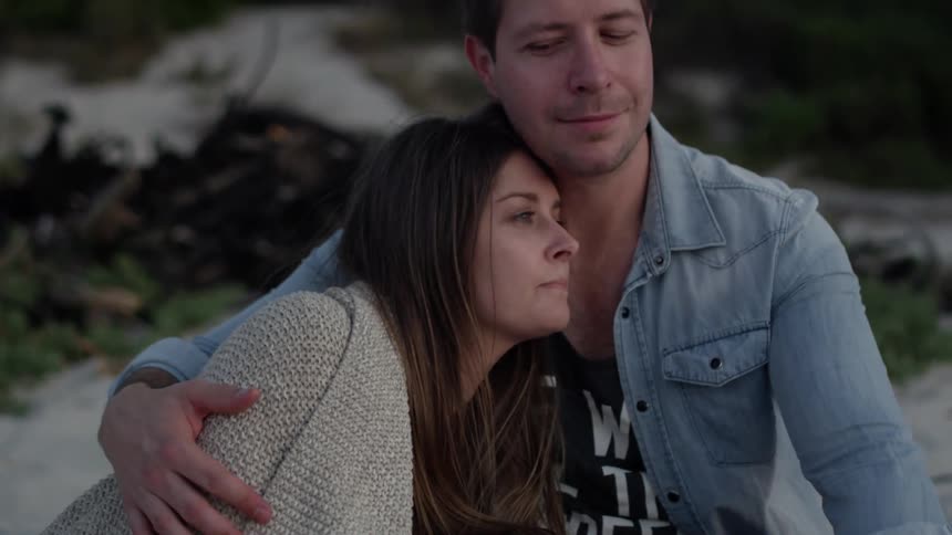 A woman kisses a man on the cheek as they sit on the beach