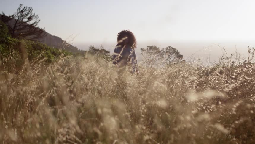 A woman is walking on a hill with tall grass on a cloudy day