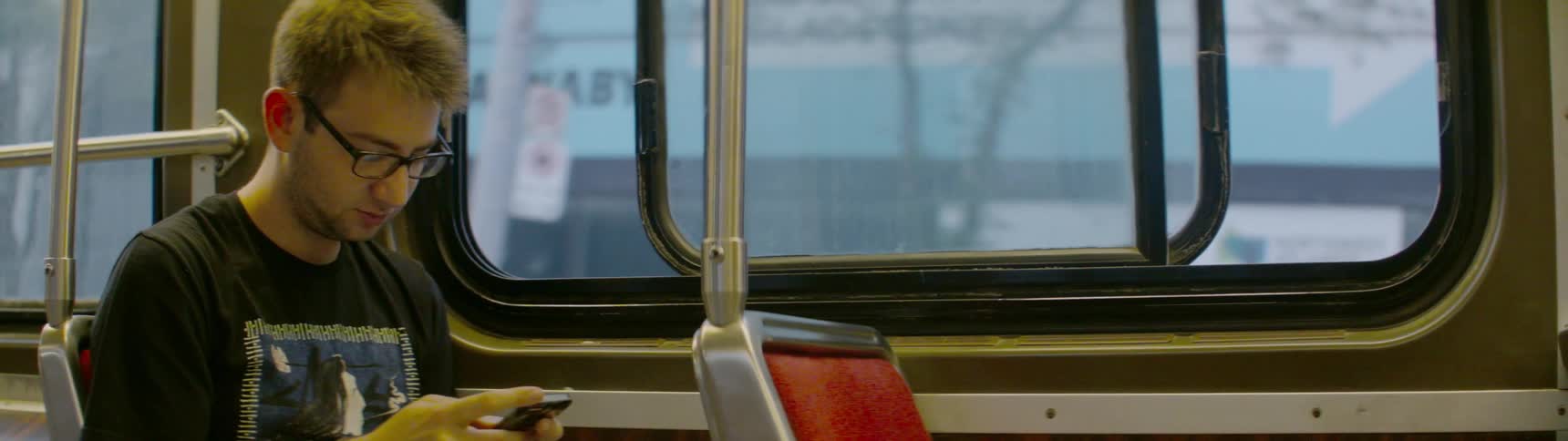 A young man sits on a bus and fiddles with a smartphone