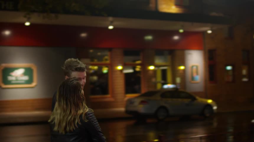 A man and woman walk and talk on an urban street at night