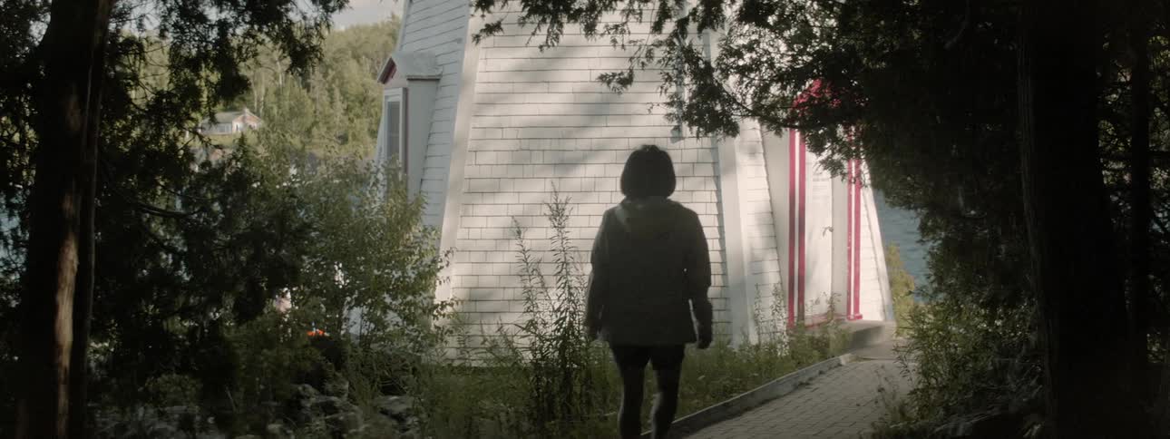 Woman walks along path under trees toward house