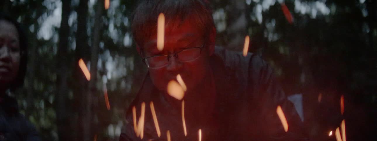 An asian man or woman stand over sparks from a fire