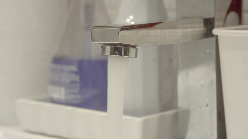 Water pours from faucet on counter near bottles and containers