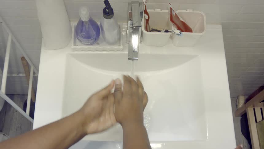 A person turns the water on at a sink and washes their hands