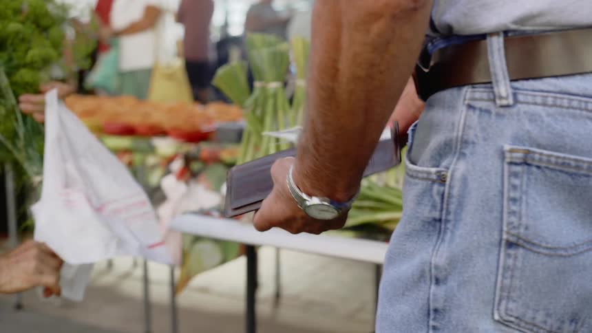 A man takes money out of his wallet standing beside a food market table