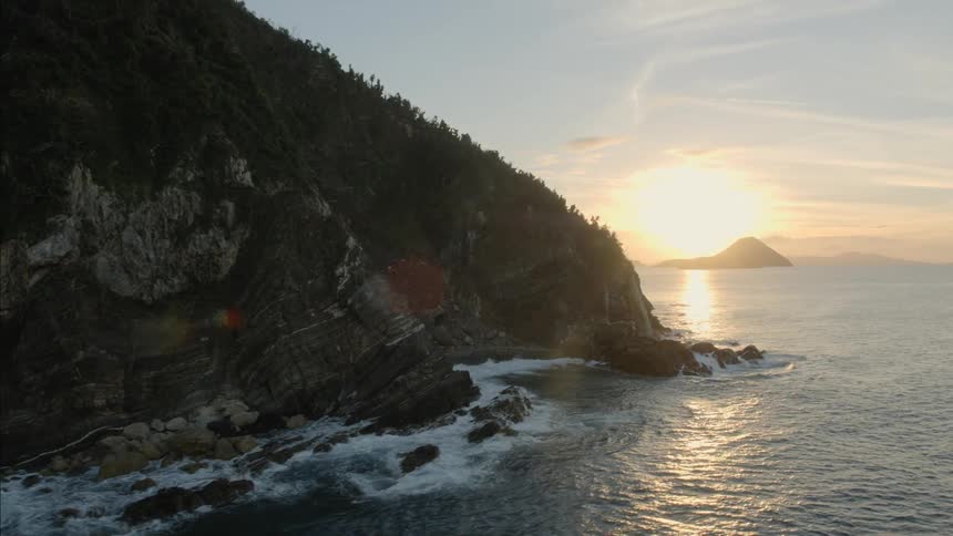 Ocean waves splash against the rocky sloped shore at sunset