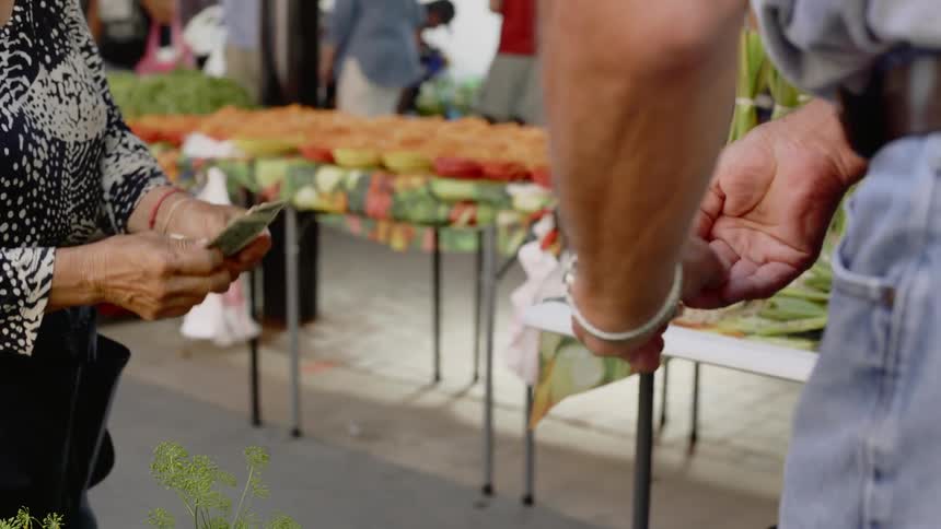 A man counts out money and hands it to a woman working at an outdoor market