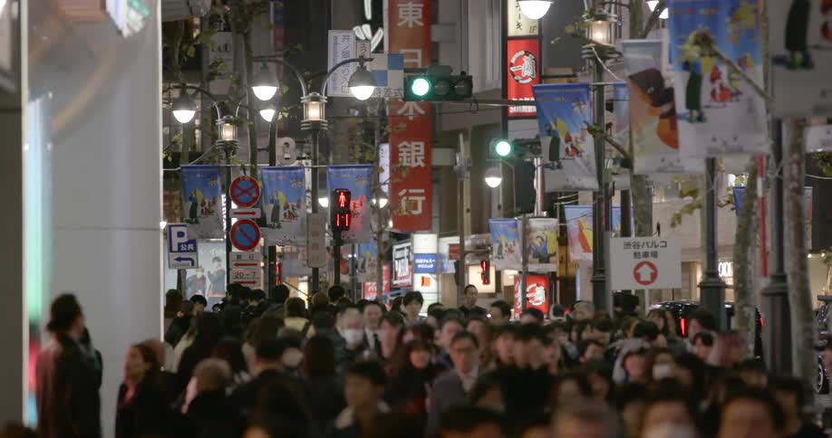 A large crowd of people walk down a busy city street in Tokyo