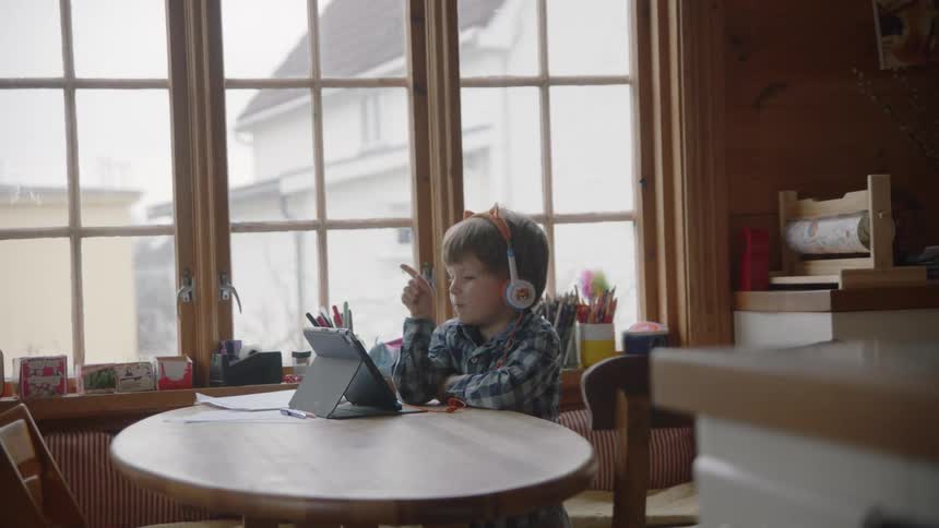 A boy sitting at a table with headphones looking at a tablet
